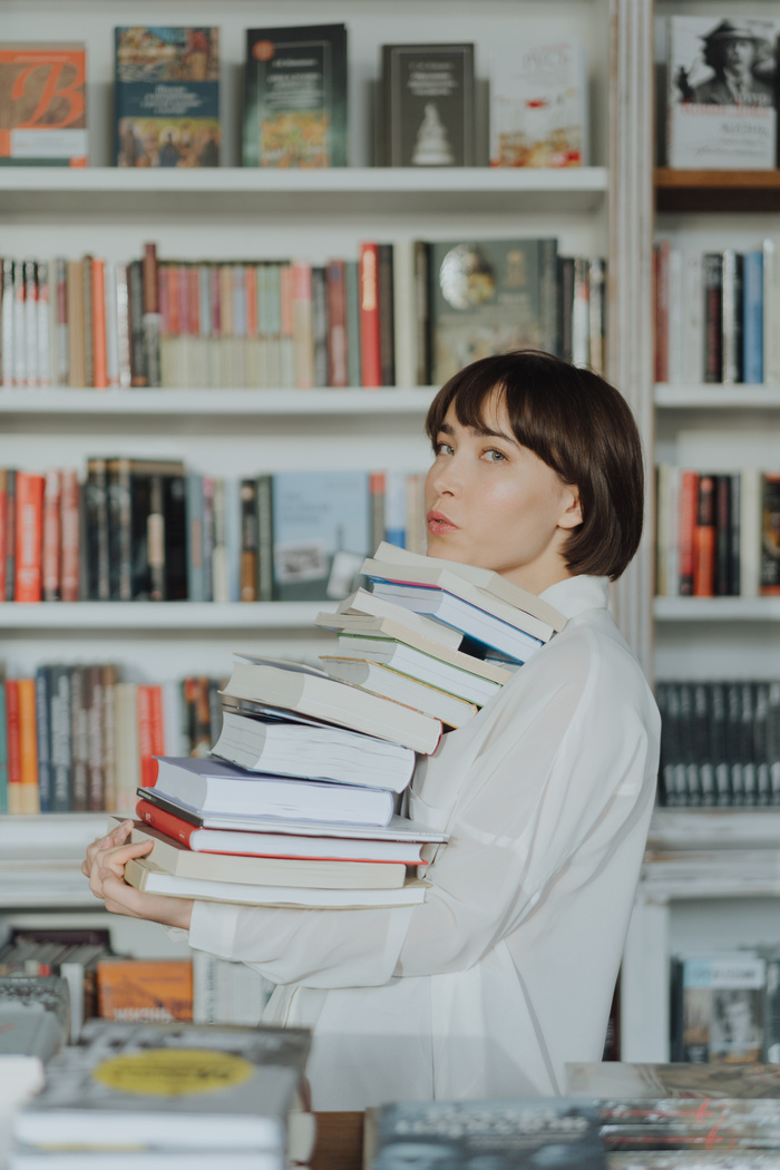 Woman in White Long Sleeve Shirt Carrying a Stack of Books