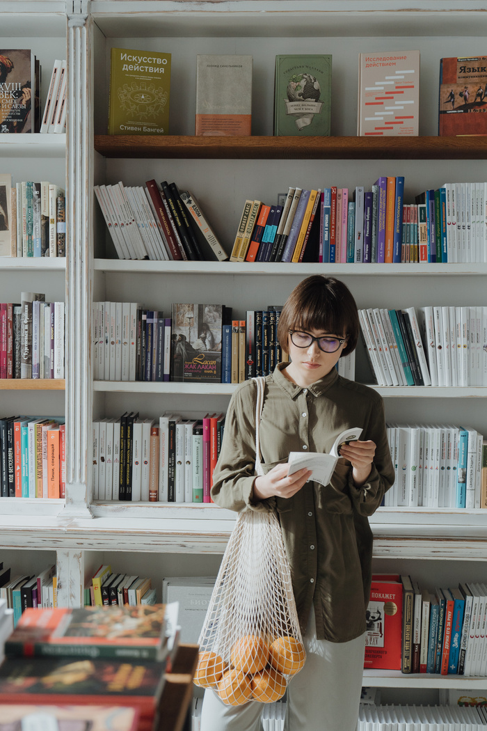 Woman in Brown Coat Standing Beside White Wooden Book Shelf